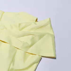 Yellow dress detail close-up, showcasing smooth fabric and elegant draped design.