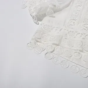 Detailed view of white embroidered lace short shirt with nautical hollow motifs and delicate trim.