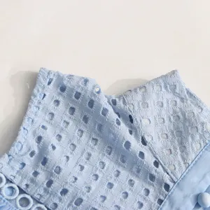 Gros plan détaillé du tissu de robe sans manches bleu clair brodé et ajouré à col montant.