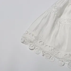 Close-up detail of white layered skirt with intricate lace embroidery and scalloped hem.