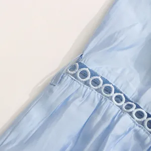 Détail en gros plan d'une robe d'été sans manches bleu clair avec broderie ajourée blanche.