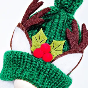 Close-up of Christmas gnome knitted hat with reindeer antlers, white ears and red pom-poms.