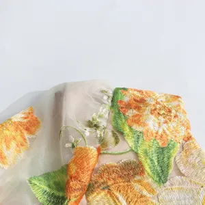 Close-up detail shot of exquisite 3D floral embroidery on elegant mesh dress fabric.
