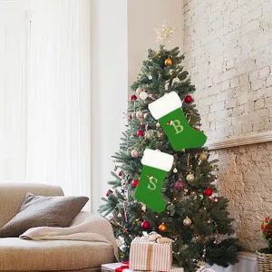 Detailansicht großer grüner Weihnachtssocken aus Samt mit bestickten Buchstaben am Tannenbaum.