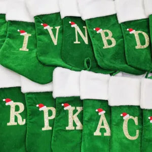 Grüner Samt-Weihnachtsstrumpf mit Glitzer-Buchstaben-Bestickung für die Feiertagsdekoration.