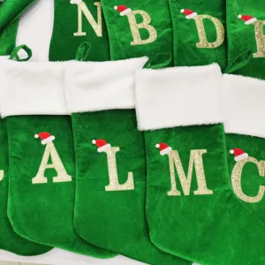 Grüne Samt-Weihnachtsstrümpfe mit weißem Plüschbündchen und Glitzer-Buchstaben für Festgeschenke.