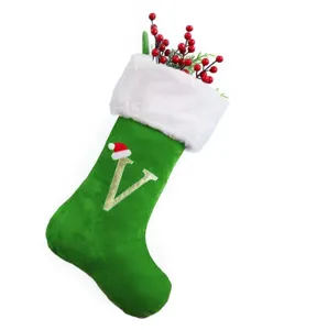 Detailaufnahme eines grünen Samt-Weihnachtsstrumpfs mit Buchstabe V und roten Beeren.