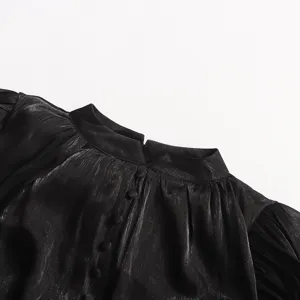 Détail de robe métallisée noire avec col montant, texture du tissu et boutons recouverts.