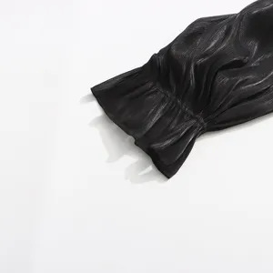 Gros plan sur le poignet de manche longue en tissu métallisé scintillant noir plissé.