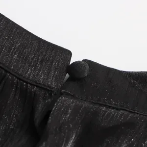Gros plan détaillé montrant le tissu noir scintillant et le bouton de la robe vintage.