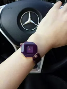 Detaillierte Handgelenkaufnahme einer Damenmodeuhr mit violettem facettiertem Glas und Armband.