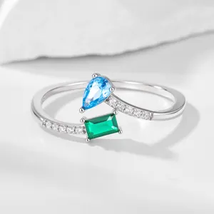 Zilveren geometrische zirkonring detailopname met elegante druppel- en smaragdstenen.