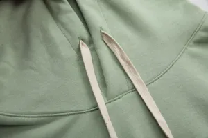 Green cotton hoodie detail close-up showing casual drawstring sweatshirt fabric texture.