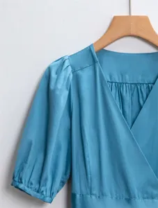 Vue détail robe bleue col V, design élégant de manches bouffantes, gros plan texture tissu.