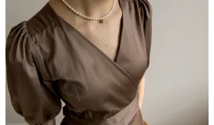 Gros plan sur la robe portefeuille à manches bouffantes française et son collier de perles.