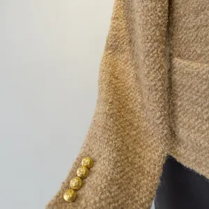 Close-up van de mouw van een tweed jasje met elegante gouden knopen en fijne textuur.