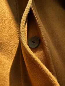Elegant cashmere blend wool coat detail shot featuring a classic button and warm camel tone.