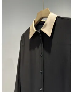 Close-up detail of the black long-sleeve blouse featuring a contrasting beige collar and buttons.
