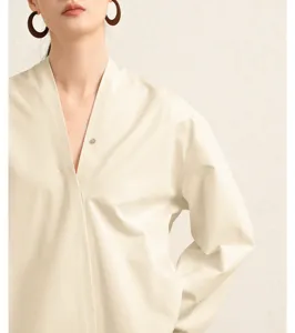 Close-up detail of women's beige cotton poplin V-neck long sleeve blouse, soft texture.