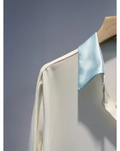 Detail of women white shirt with contrast light blue satin collar hanging on wood hanger.