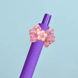 Close-up of cute pink glitter bow and flower charm detail on purple gel pen tip design.