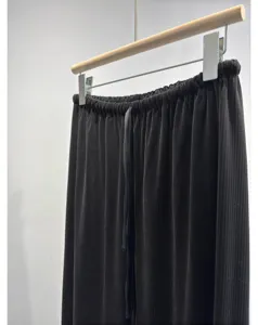 Detailed close-up of black pleated trousers with elastic waist and drawstring detail.
