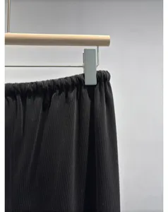 Close-up detail of black pleated elastic waist pants hanging on wooden hanger against plain wall