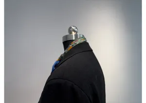 Detailopname van de kraag van een zwarte damesblazer met een gekleurde zijden sjaal.