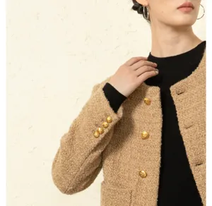 Gedetailleerde close-up van een beige tweed jasje voor dames met gouden knopen.
