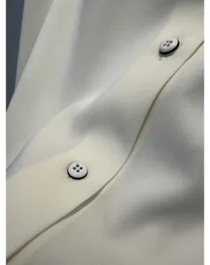 Close-up detail of smooth white silk blouse fabric with elegant contrast buttons.