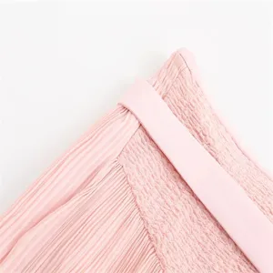 Pink pleated skirt detail view showcasing elastic smocked high waist and fine pleats texture.