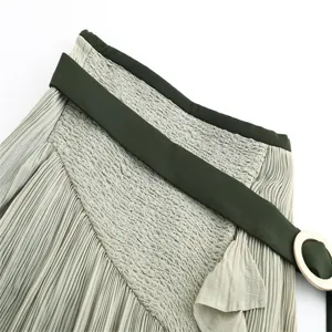 Detailed shot of pleated skirt waist featuring green belt and elastic smocked high waist.