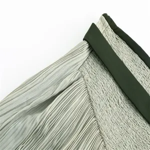 Close-up detail of pleated skirt fabric and contrasting waist band, elegant sage green texture.