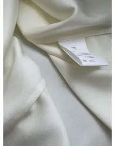 White silk fabric detail shot showcasing smooth texture, premium quality material and wash label.