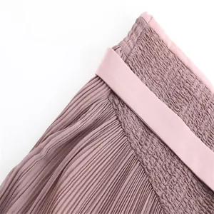 Close-up detail of women's pink high-waisted pleated midi skirt with smocked elastic waistband.