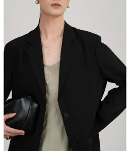 Detailopname van een elegante zwarte blazer met parelketting en chique zwarte tas.