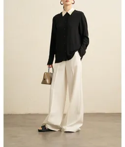 Detailed view of elegant black long-sleeve blouse with contrasting white collar and wide pants.