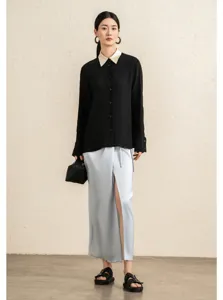 Detailed shot of model wearing a chic black blouse with contrast collar and sleek satin skirt.