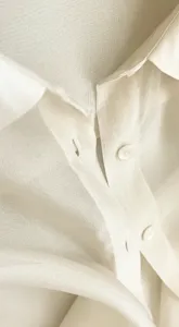 Close-up detail of an elegant translucent white organza shirt collar and buttons for women.