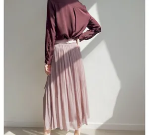 Detailed view of women's high-waist pleated skirt and long sleeve blouse in soft light.