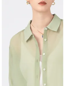 Sheer green organza shirt detail, elegant gold hoop earrings and minimalist necklace.