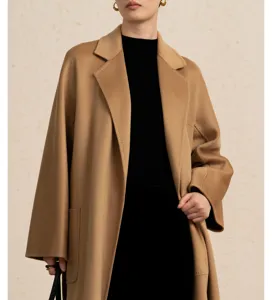 Detail shot of a luxurious camel long cashmere coat worn with a black top and gold earrings.