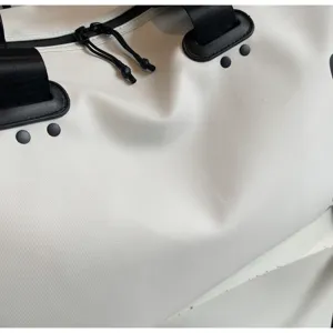 Close-up detail van witte reistas met duurzame stof, zwarte riemen en ritssluitingen.
