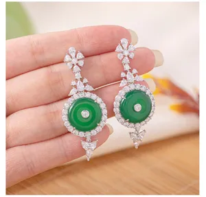 Close-up detail shot of exquisite green chalcedony and paved zircon dangle earrings on hand.