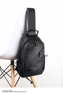 Close-up detail of a minimalist black men chest bag hanging on a white chair, sleek zipper.