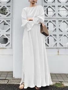 Detailed view of white pleated long dress fabric and elegant drape on model in outdoor setting.