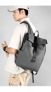 Detail view of grey roll-top backpack with black straps worn by model for daily commute use.