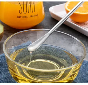 Nahaufnahme eines langen Edelstahl-Rührlöffels beim Rühren von Sirup in einer Glasschüssel.