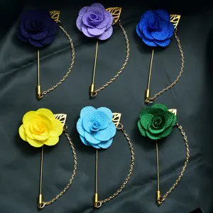 Close-up detail of multi-color fabric camellia lapel pins with metal chain and leaf decor.