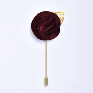 Détail de boutonnière rose en tissu bourgogne, tige et feuille élégantes en métal doré.